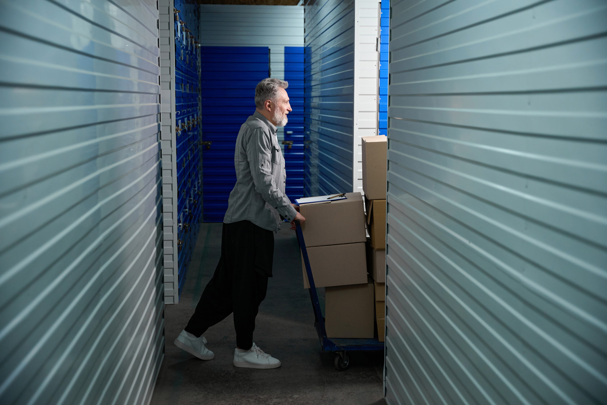 Adult man standing near big trolley with stacked boxes in storehouse and walking