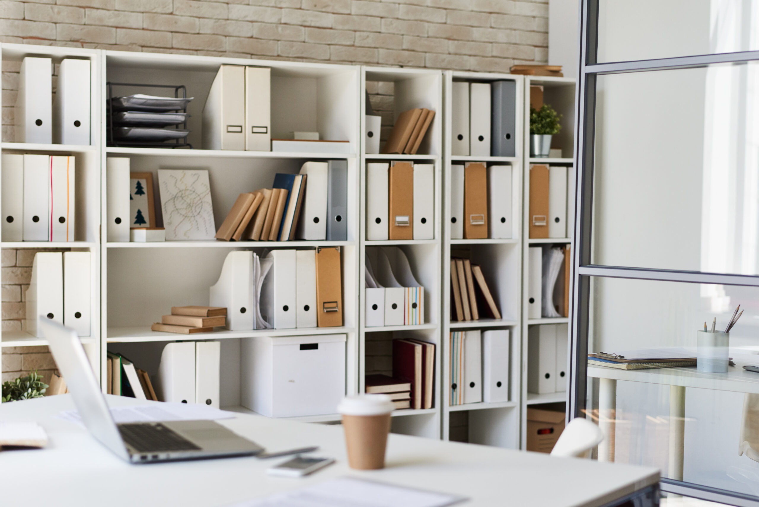 Background image of empty workplace with laptop, coffee cup and documents on desk in modern white office