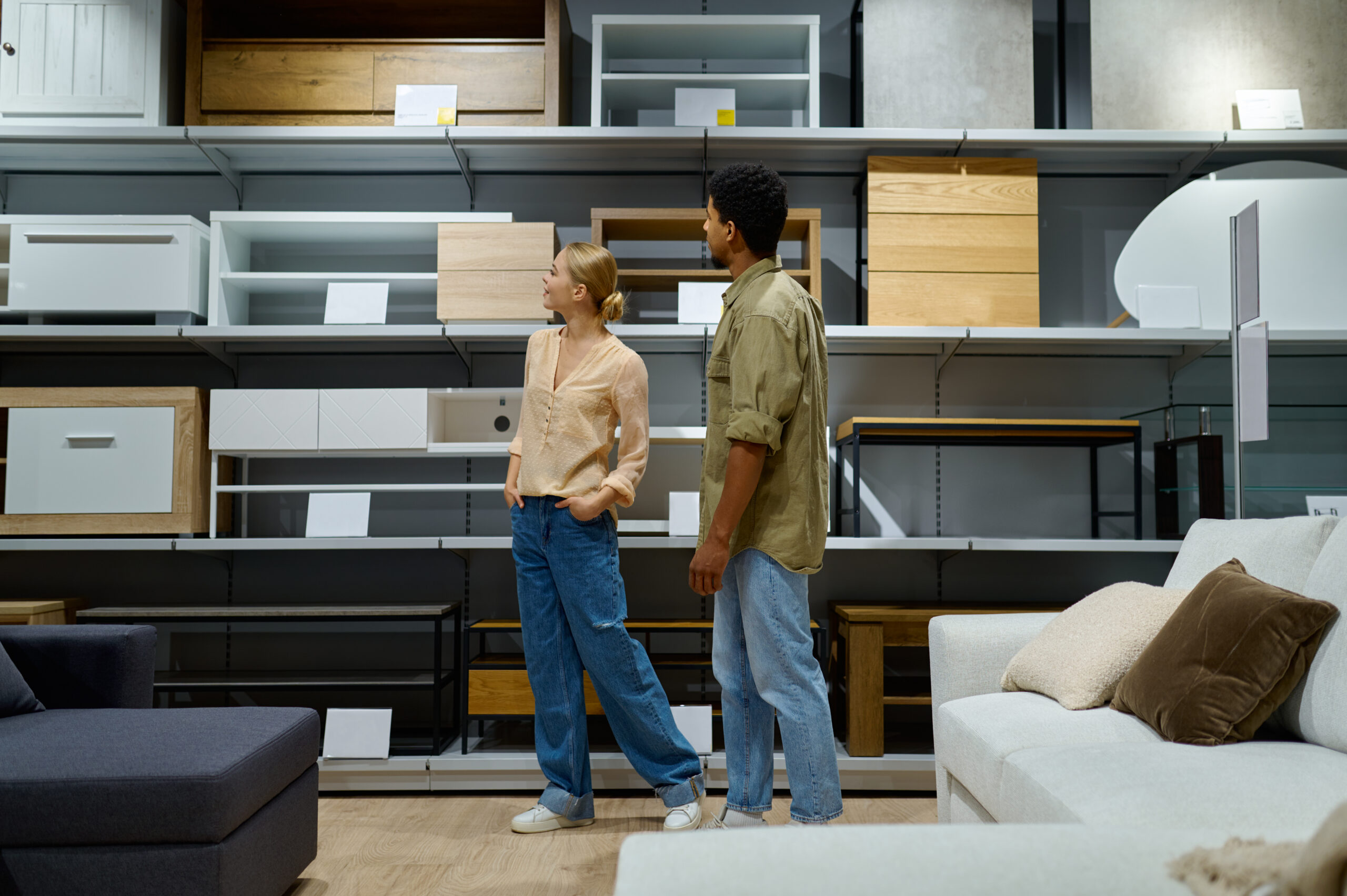 Young multiracial married family couple considering furniture store assortment on shelves showcase